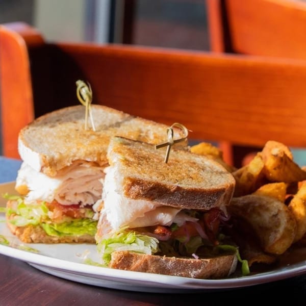Two Wyld Pines turkey club sandwiches with lettuce, tomato, and chips on a white plate.