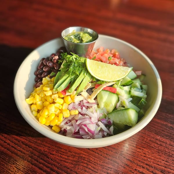 A colorful Wyld Pines American salad bowl with corn, beans, avocado, and lime on a wooden table.