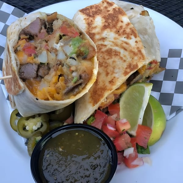 Two large burritos, one cut open, revealing steak, cheese, and vegetables, with salsa and lime.