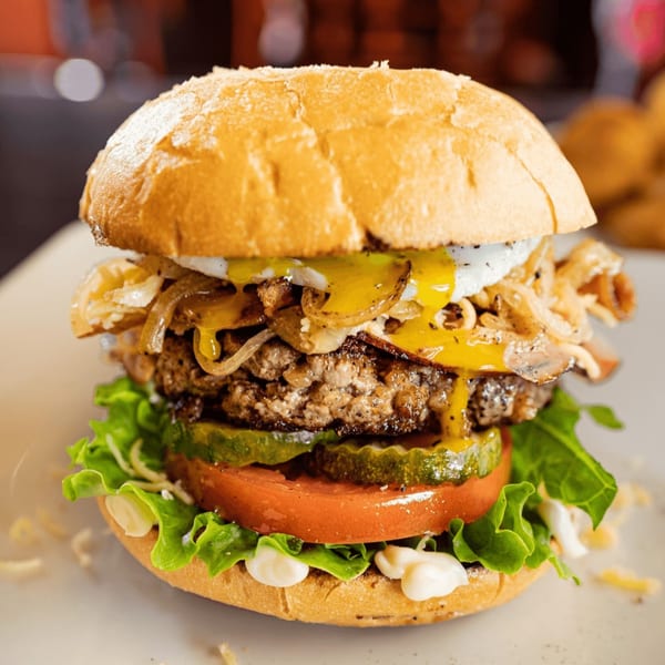 A Wyld Pines burger with a fried egg, melted cheese, caramelized onions, lettuce, tomato, and pickles.