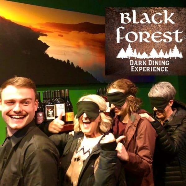 Four people, three blindfolded, smiling and laughing during a "Black Forest Dark Dining Experience" at Wyld Pines.